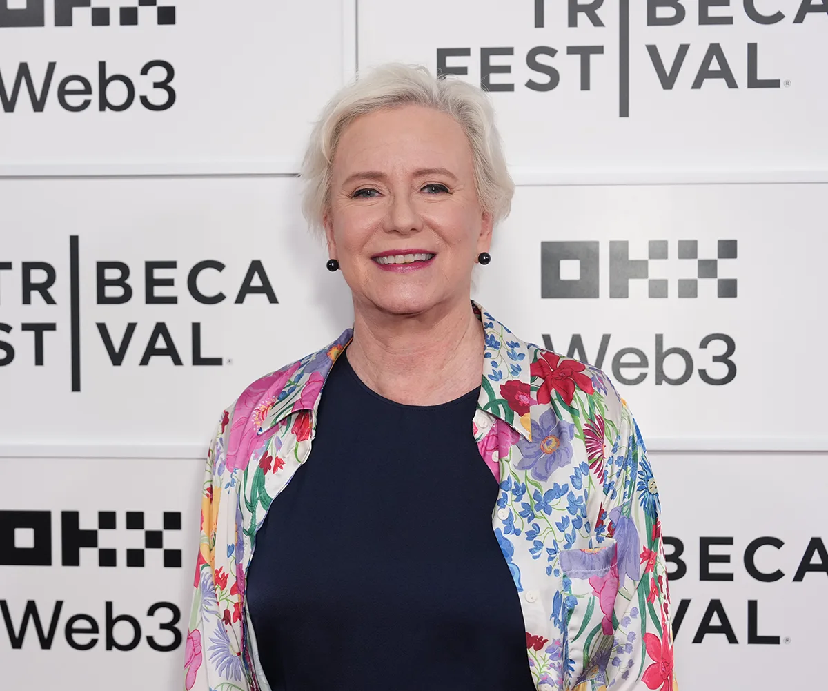 Eve Plumb, wearing a black top and patterned shirt, poses at an event