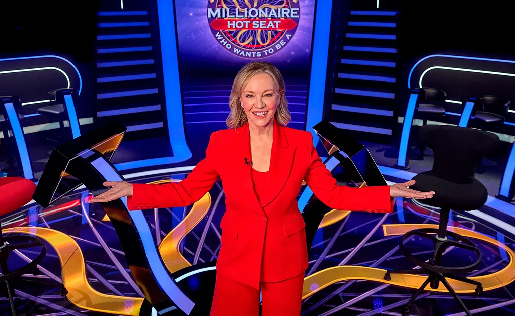 Rebecca, in a red suit, poses on the set of Millionaire Hot Seat.