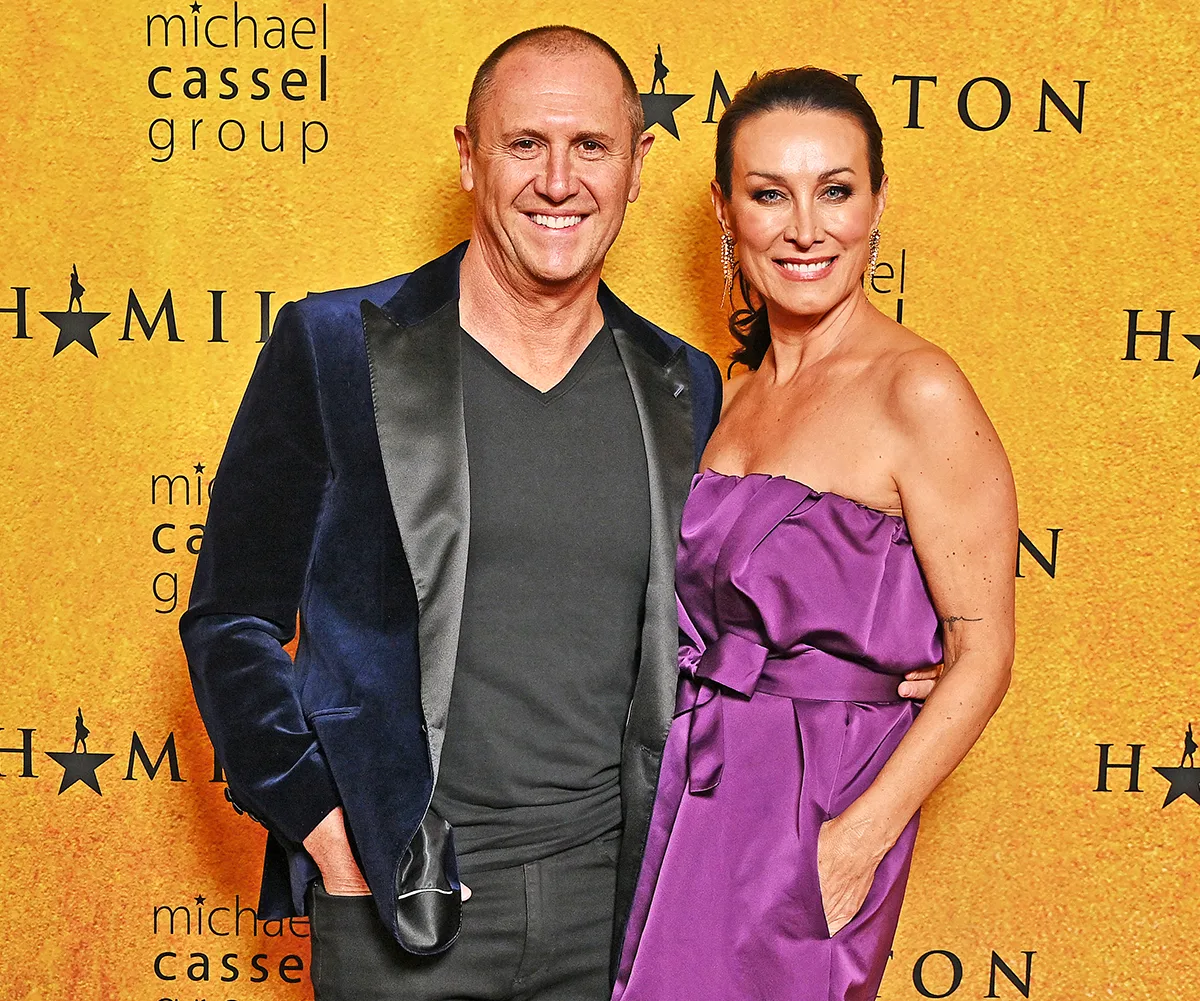 Larry, in a black suit, stands with his arm around his wife Sylvie, in a purple dress, at the opening night of Hamilton in Sydney.