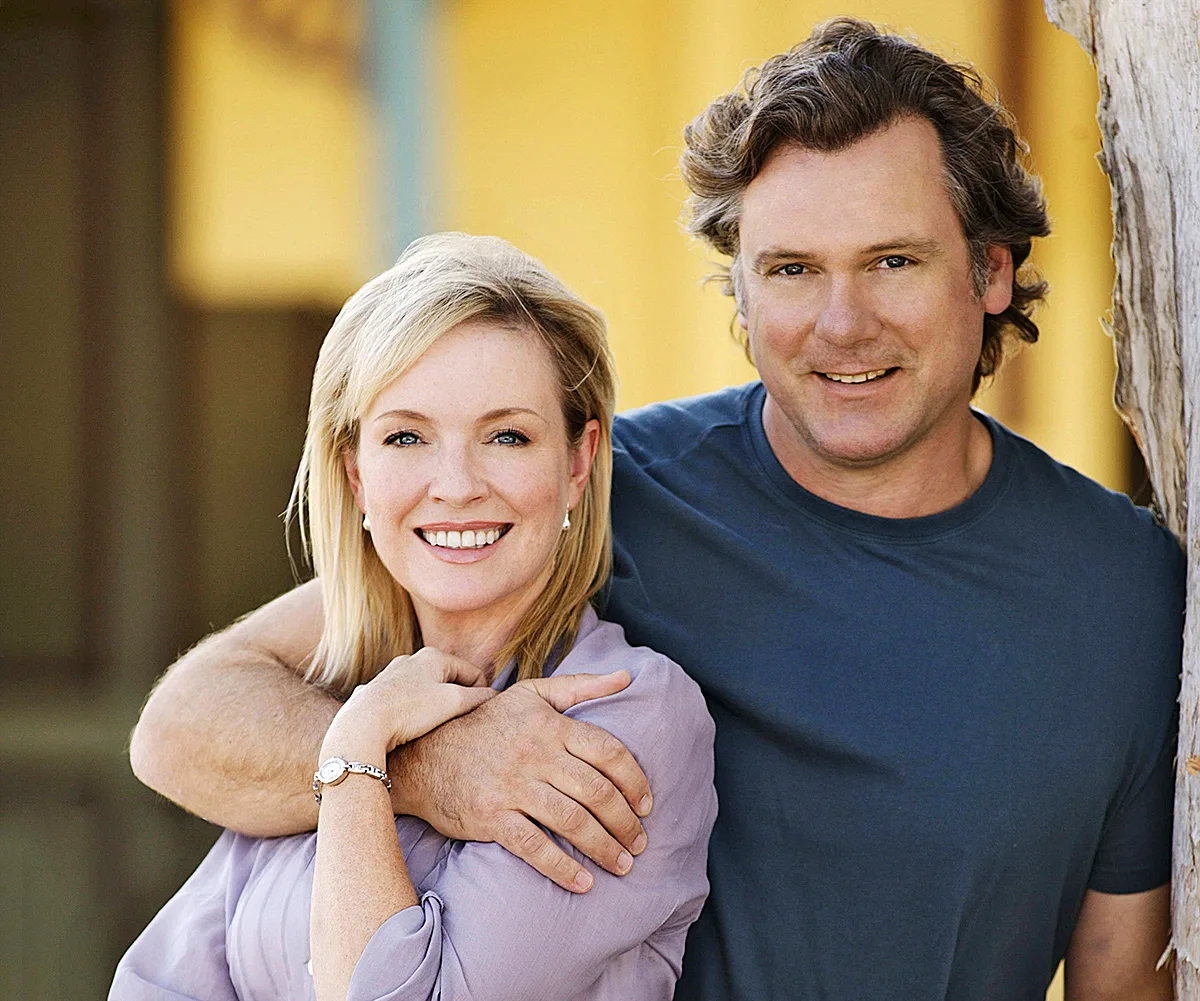 Erik Thomson, in a dark top, stands behind Rebecca, with his arm around her, on the set of Packed To The Rafters