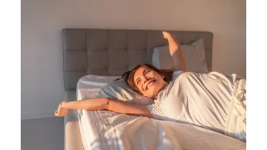 A woman smiles and stretches in bed as the morning light pours in.