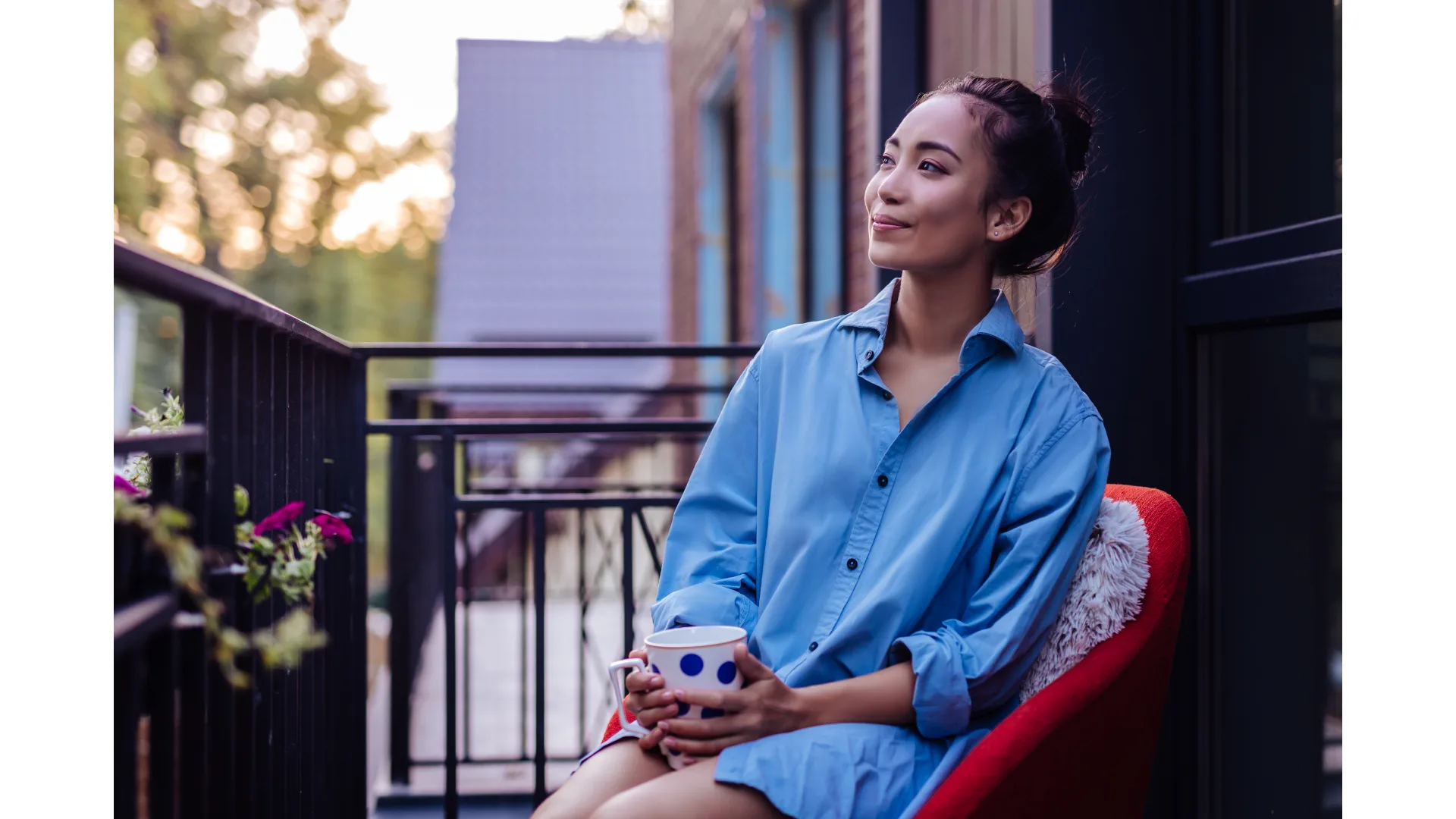 A woman sits outside in a blue shirt while cradling a mug and taking a quiet moment.