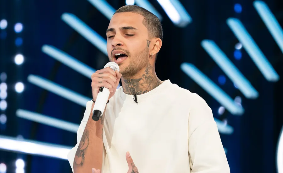 Tre, wearing a shite shirt, is singing into a microphone on the Australian Idol audition stage