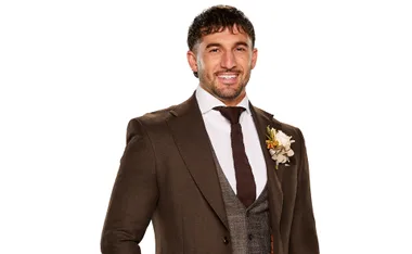 Luke Fourniotis in a brown suit smiling for a promotional shot for the latest season of Married at First Sight Australia.