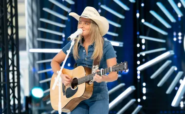 Lily-Grace Grant auditioning for Australian Idol 2026. She wears a denim jumpsuit, cowboy hat and holds a guitar.