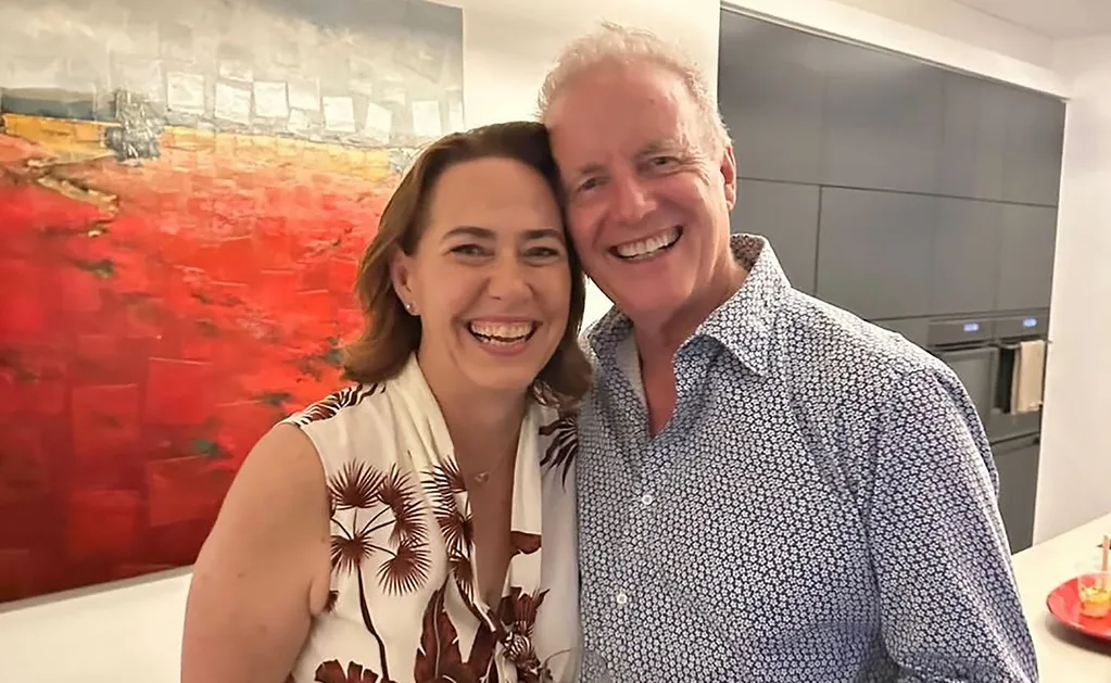 Lisa and Simon, standing close, both smiling, with a picture on the wall behind them