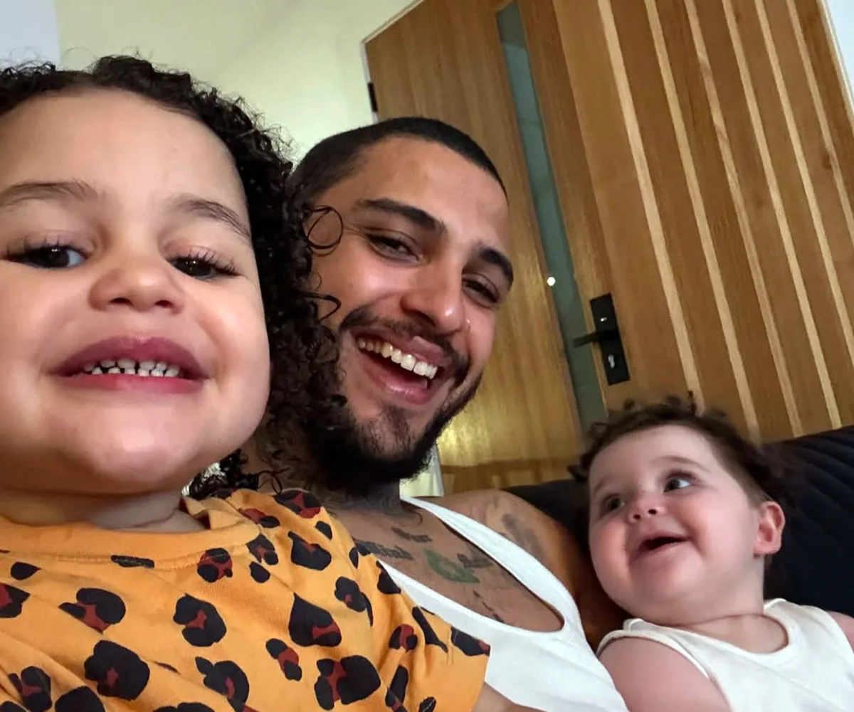 Tre smiles, with a toddler daughter on one side and a baby daughter on the other