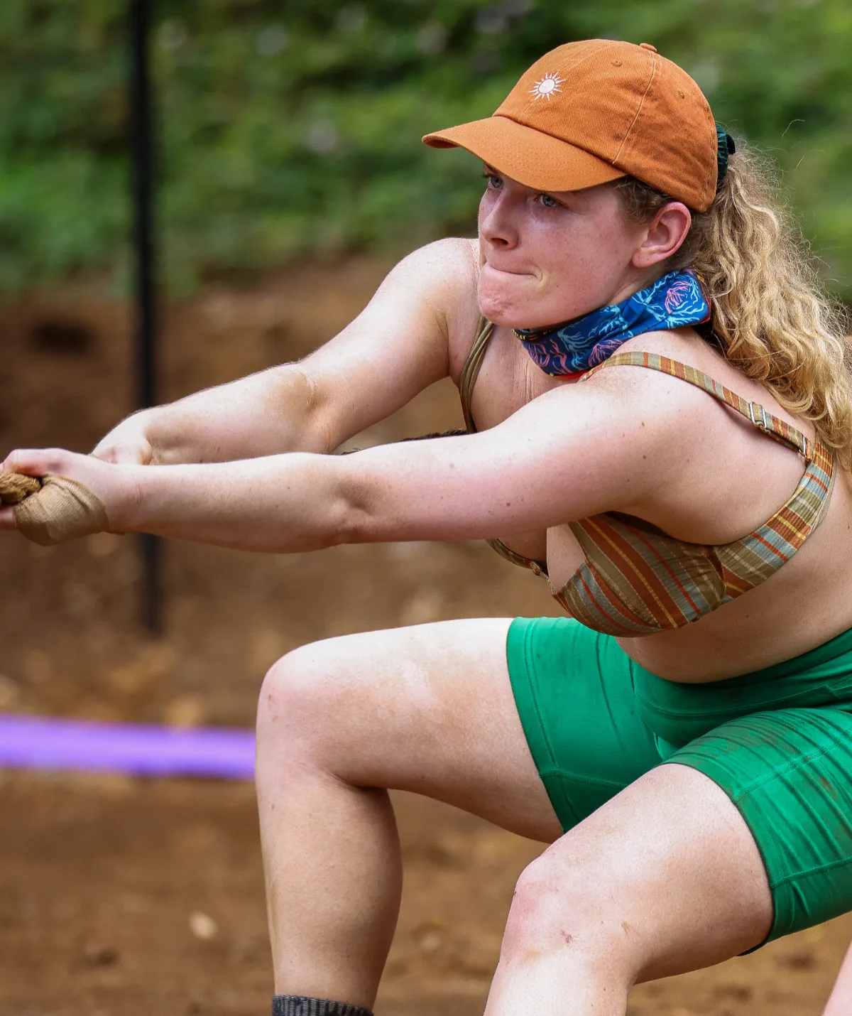 Paula, wearing green shorts, a bikini top and an orange cap, pulls on a rope during a challenge