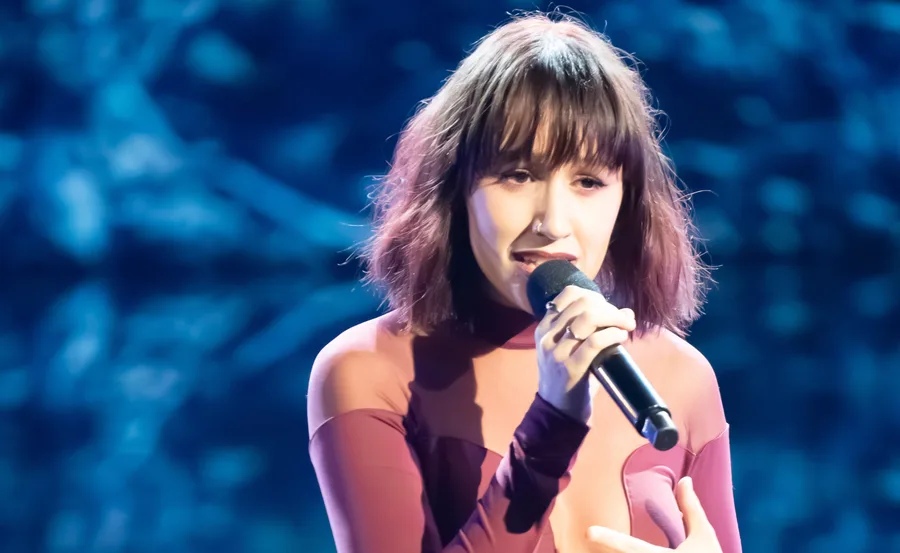 Jacinta from Australian idol on stage in a maroon set singing.