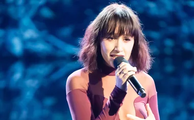 Jacinta from Australian idol on stage in a maroon set singing.