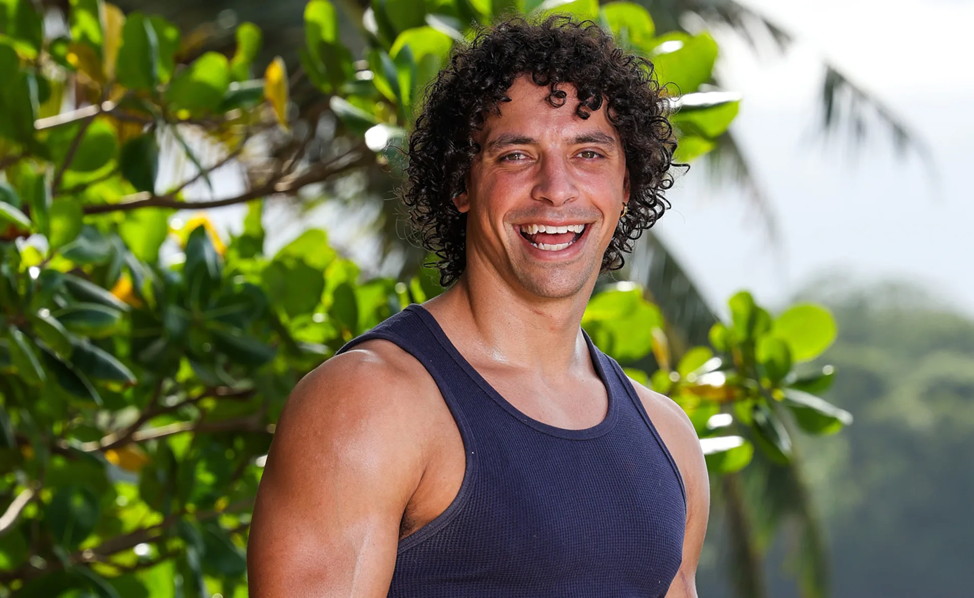Ben, wearing a dark singlet, smiles on a beach in Samoa