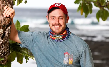 Harry, wearing a grey t-shirt, stands in Samoa with the beach in the background
