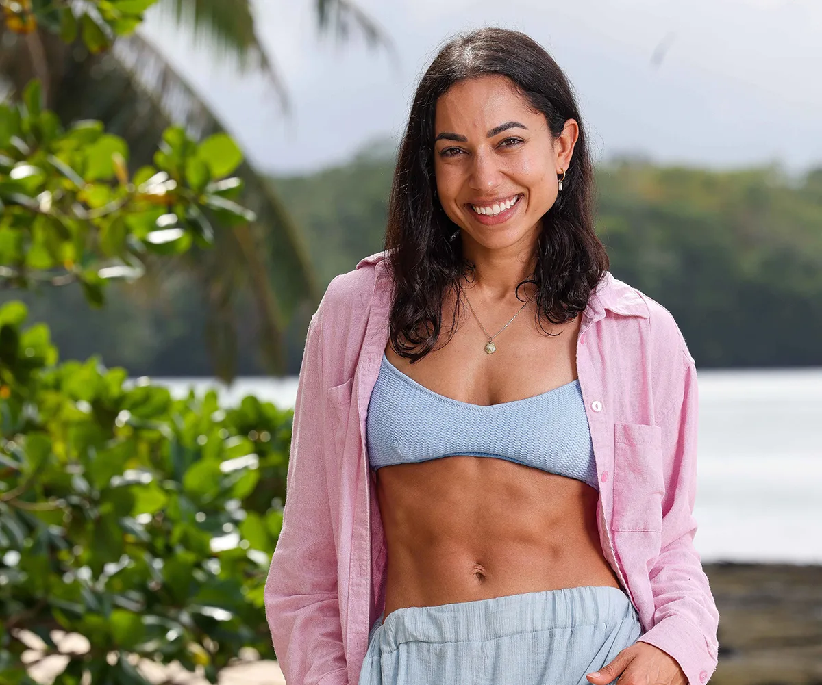 Brooke, wearing a pale blue top and a pink shirt, stands on a beach in Samoa