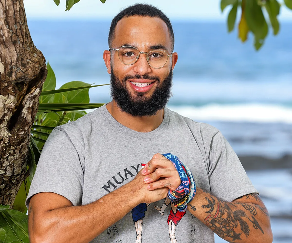 Cameron, wearing a grey t-shirt, stands on a beach in Samoa