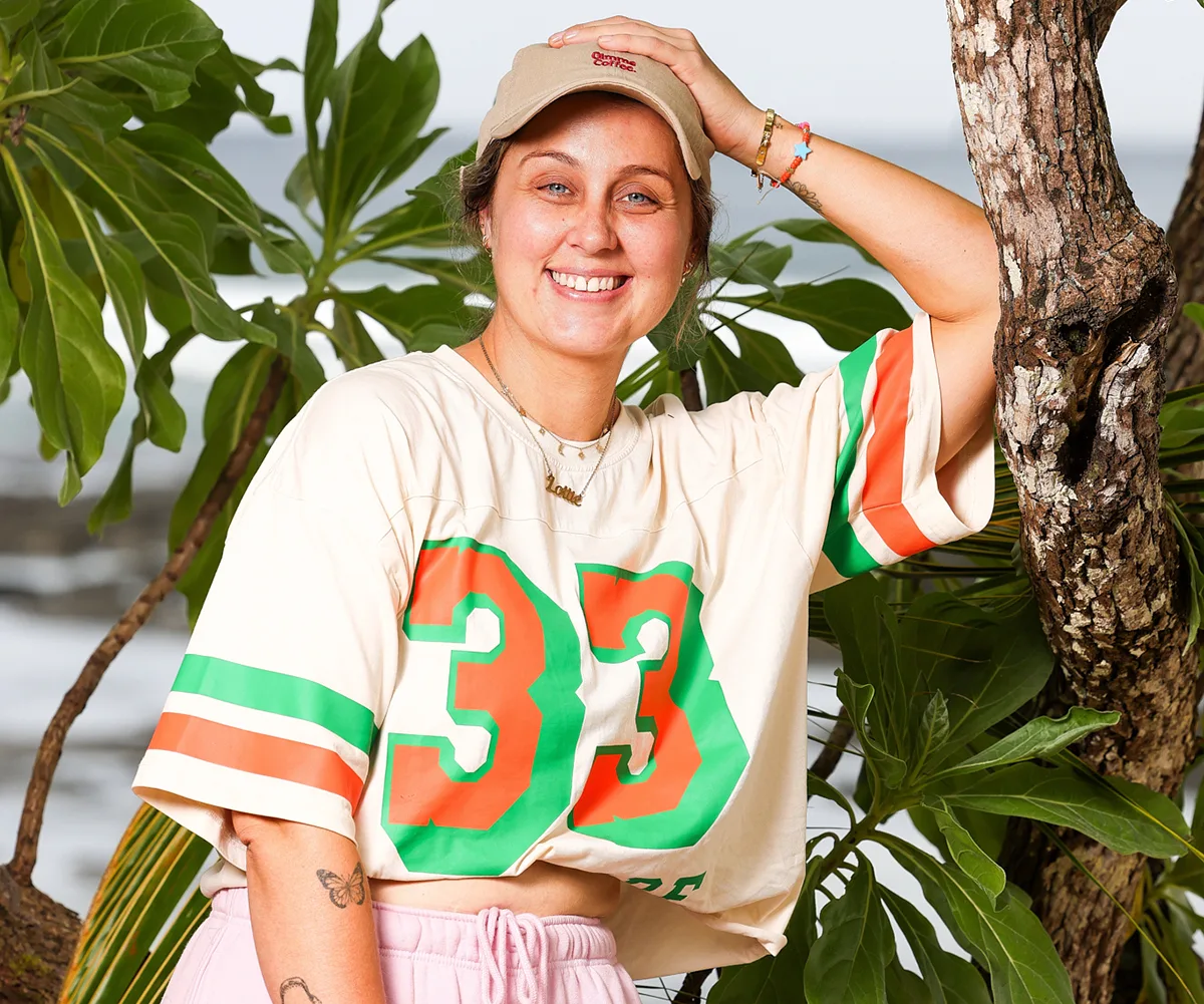 Lottie, wearing a top with the number 33 on it, smiles with her hand on her cap