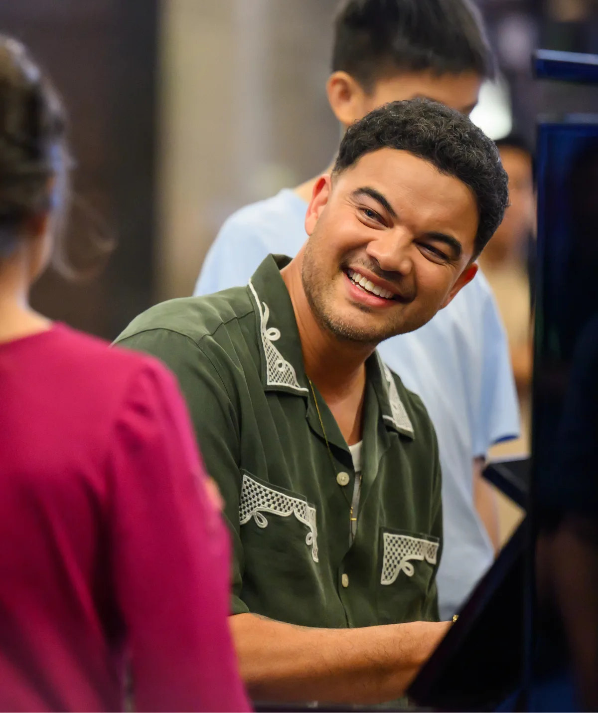 Guy, in a green shirt, smiles as he sits at the piano