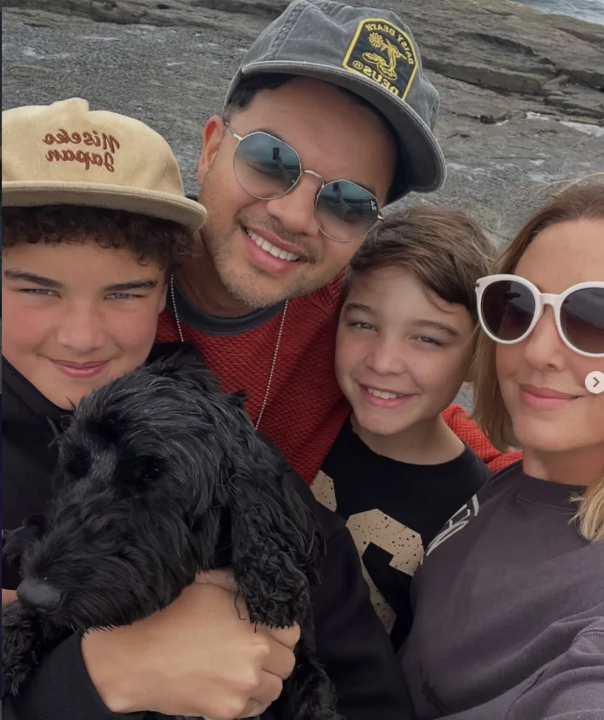 Guy, wearing a hat and sunglasses, is pictured with wife Jules, wearing sunglasses, and their sons Hudson and Archie and a black dog