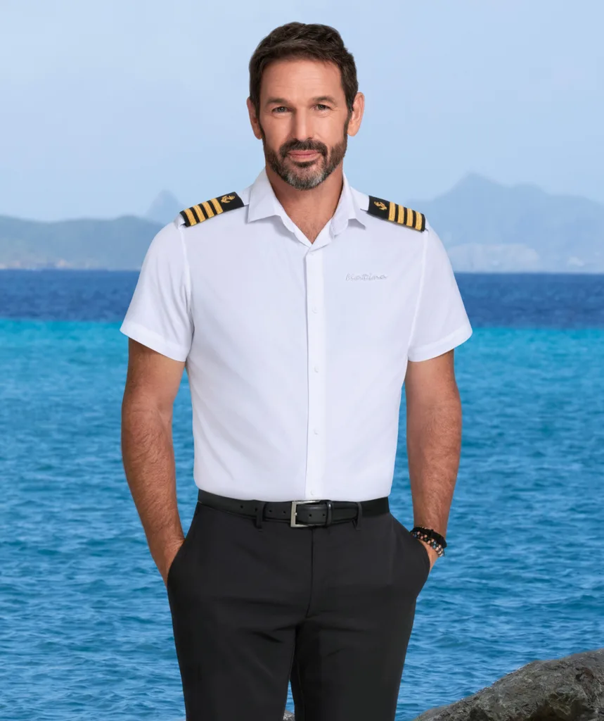 Captain Jason Chambers from Below Deck in front of the ocean in his uniform.