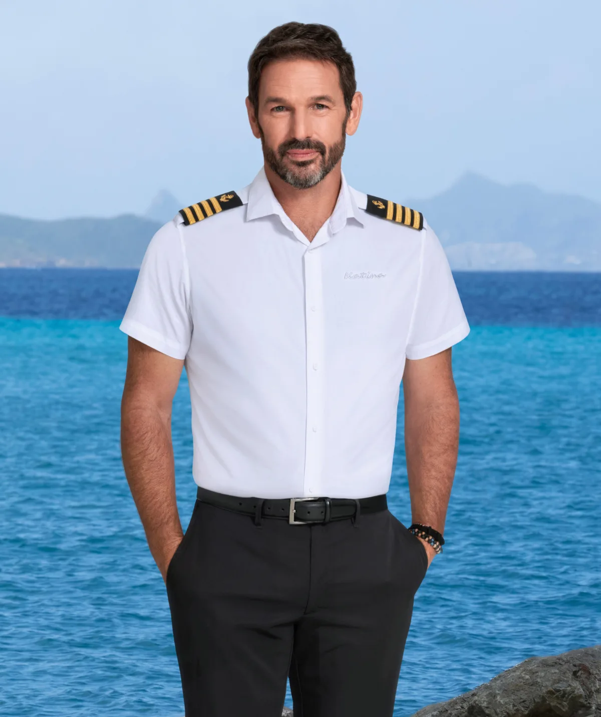 Captain Jason Chambers from Below Deck in front of the ocean in his uniform.