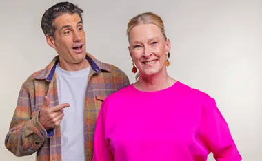 Andy Lee, wearing a white t-shirt and a checked shirt, points at Leigh Sales, in hot pink