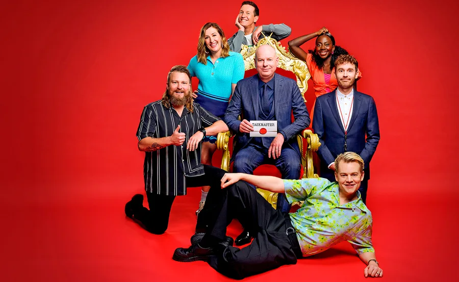 Tom Gleeson sits on a chair, surrounded by the five comedians competing on this season of Taskmaster Australia