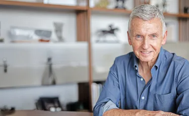Bruce McAvaney, wearing a blue shirt, sits in front of a shelf at his home