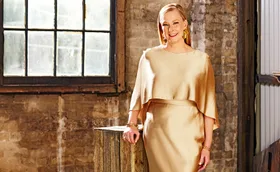 Leigh Sales, dressed in gold, stands in front of a window