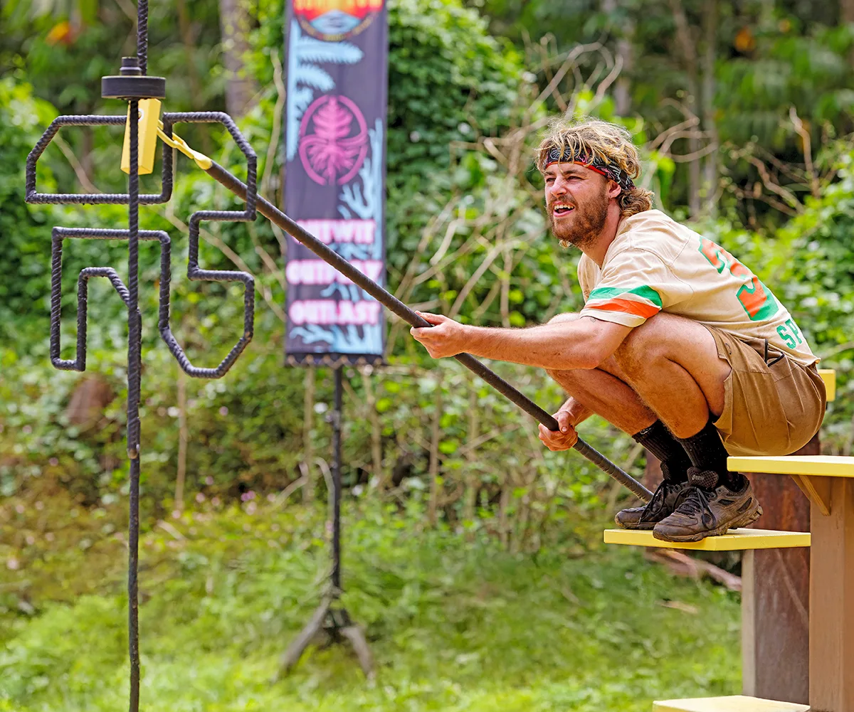 Jackson crouches, holding a long stick, in a Survivor challenge