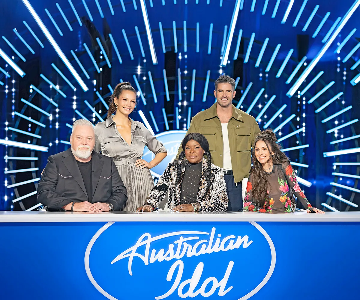 Australian Idol hosts Ricki-Lee and Scott Tweedie standing behind the three judges at their desk, Kyle Sandilands, Marcia Hines and Amy Shark.