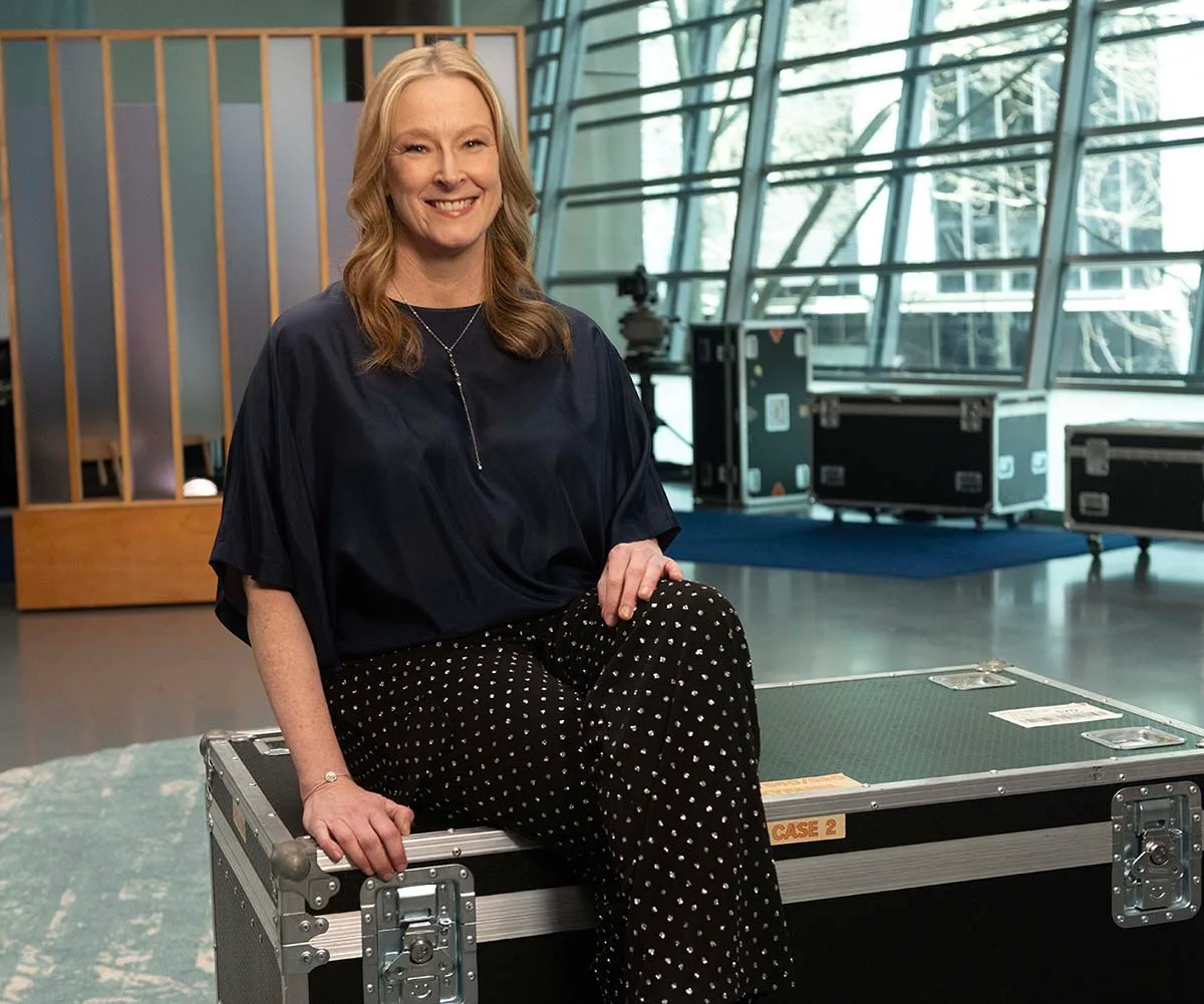 Leigh, dressed in black, sits on the set of The Assembly