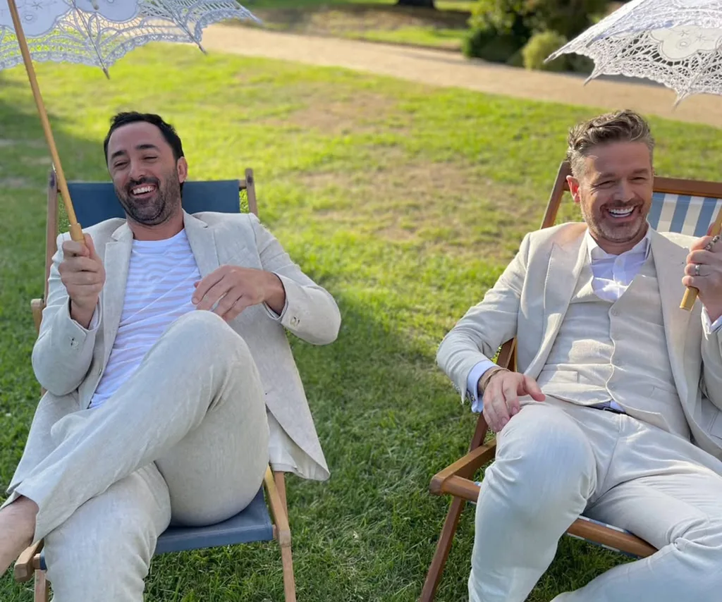 Andy Allen and Jock Zonfrillo both wearing all white in sun lounges holding parasols.