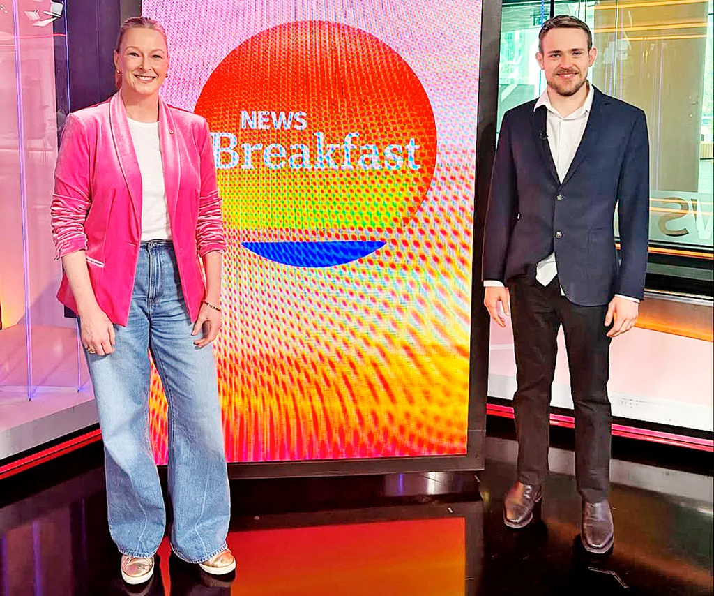 Leigh, in a pink jacket and blue jeans, stands on the set of ABC News Breakfast