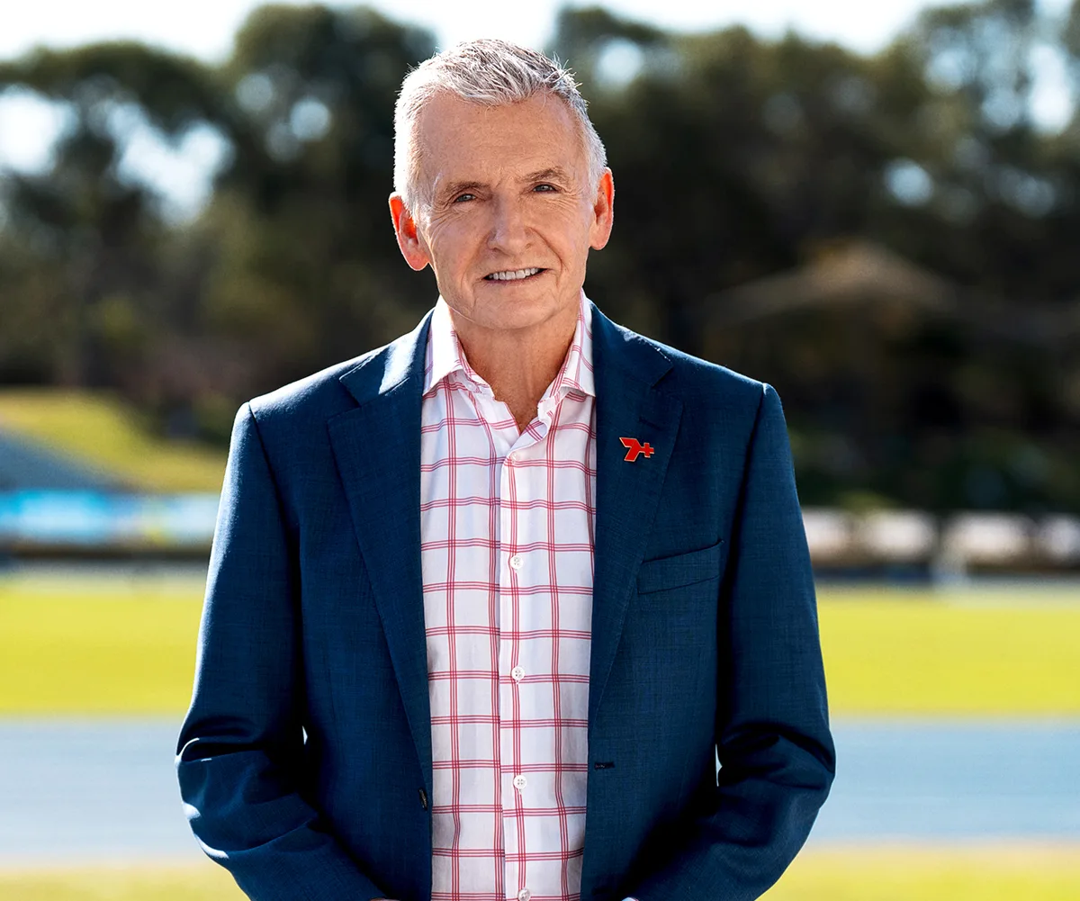 Bruce stands in front of an athletics track, wearing a dark blue jacket