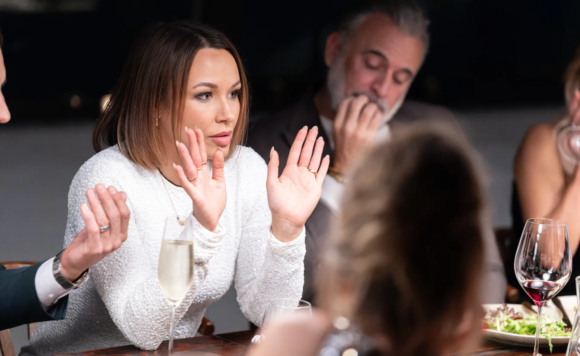 MAFS' Stella with her hands up at the dinner party table looking upset in a white dress while feuding with her co-stars.