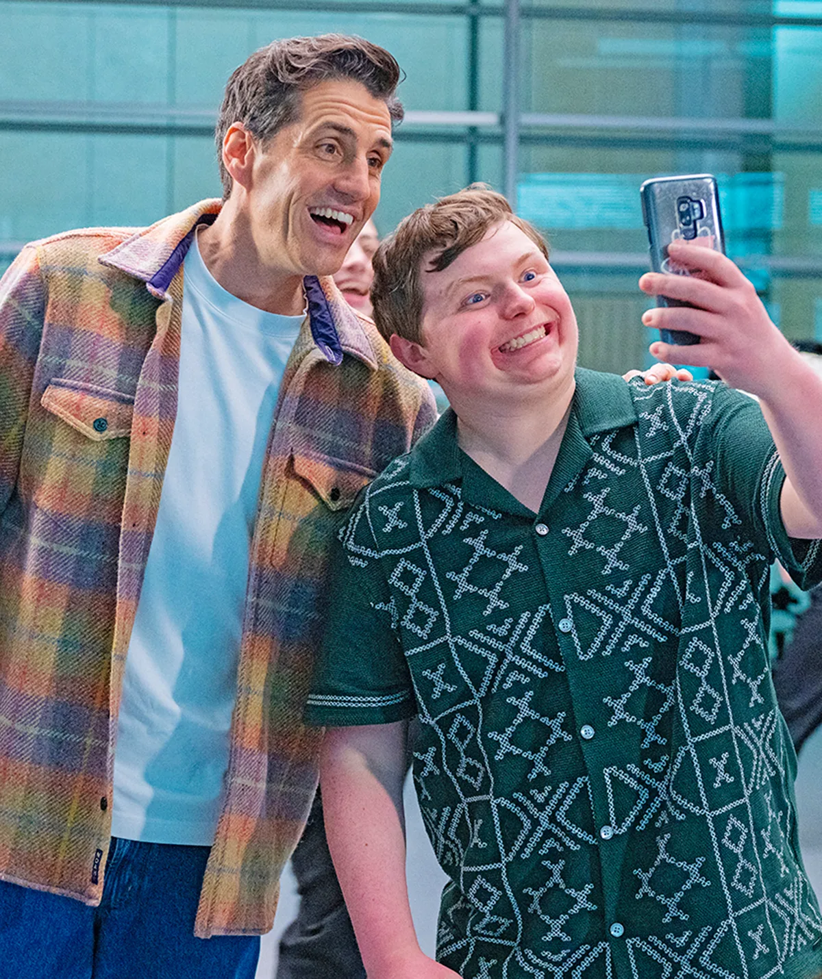 Fletcher, in a green patterned shirt, smiles as he poses for a selfie with Andy Lee