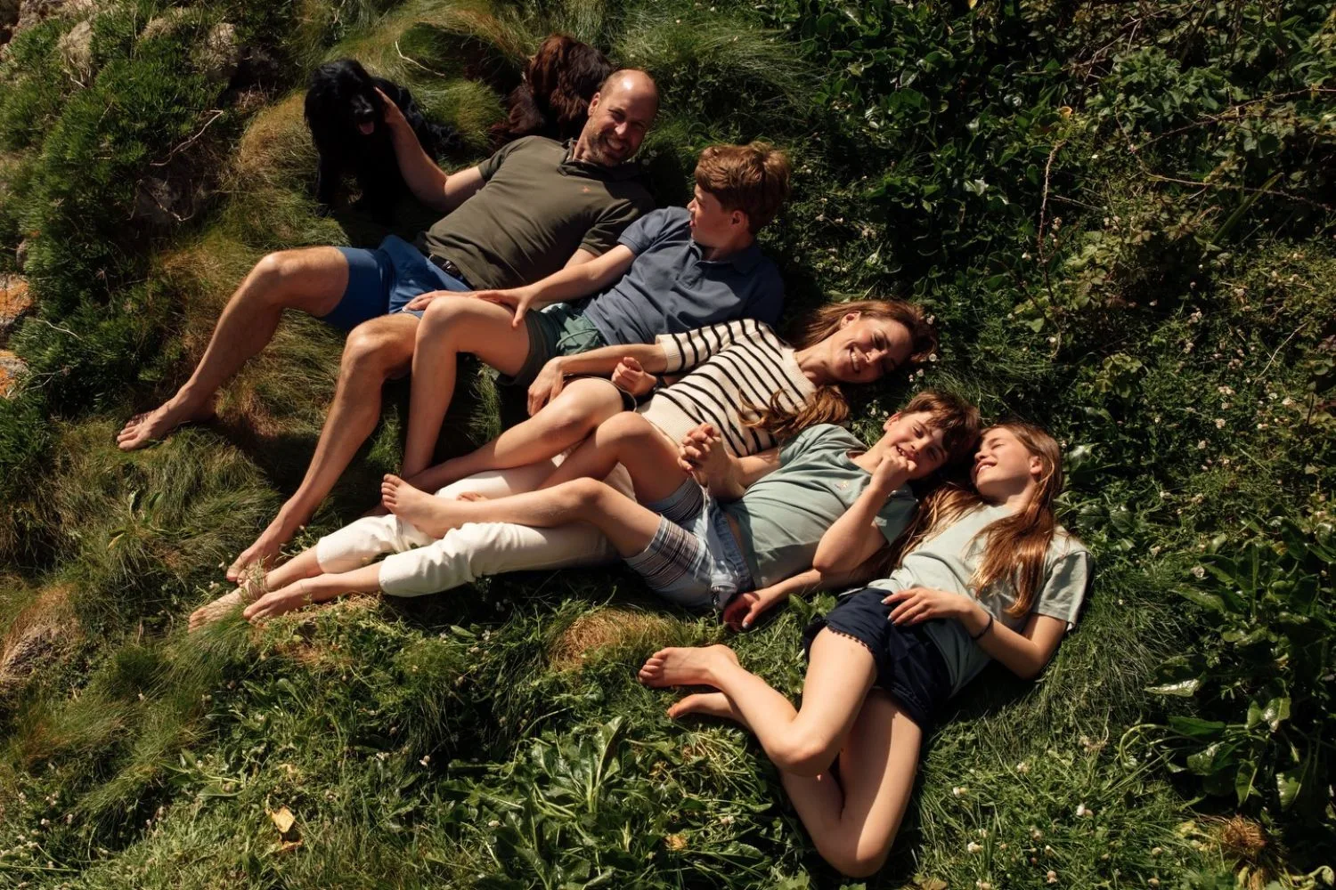 Prince WIlliam, Kate with George, Charlotte and Louis lying on a patch of grass