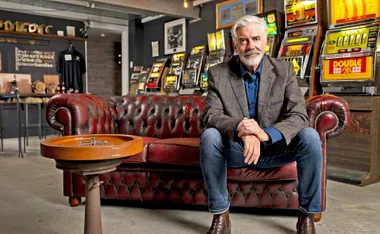 Shaun sits on a leather couch with poker machines behind him