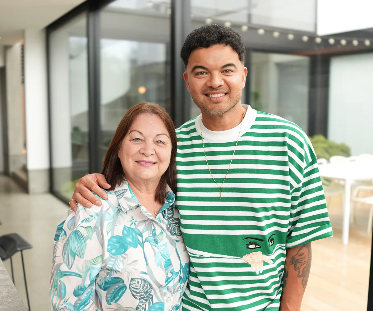 Guy, in a green striped top, stands next to his mother Nellie, in a green patterned outfit