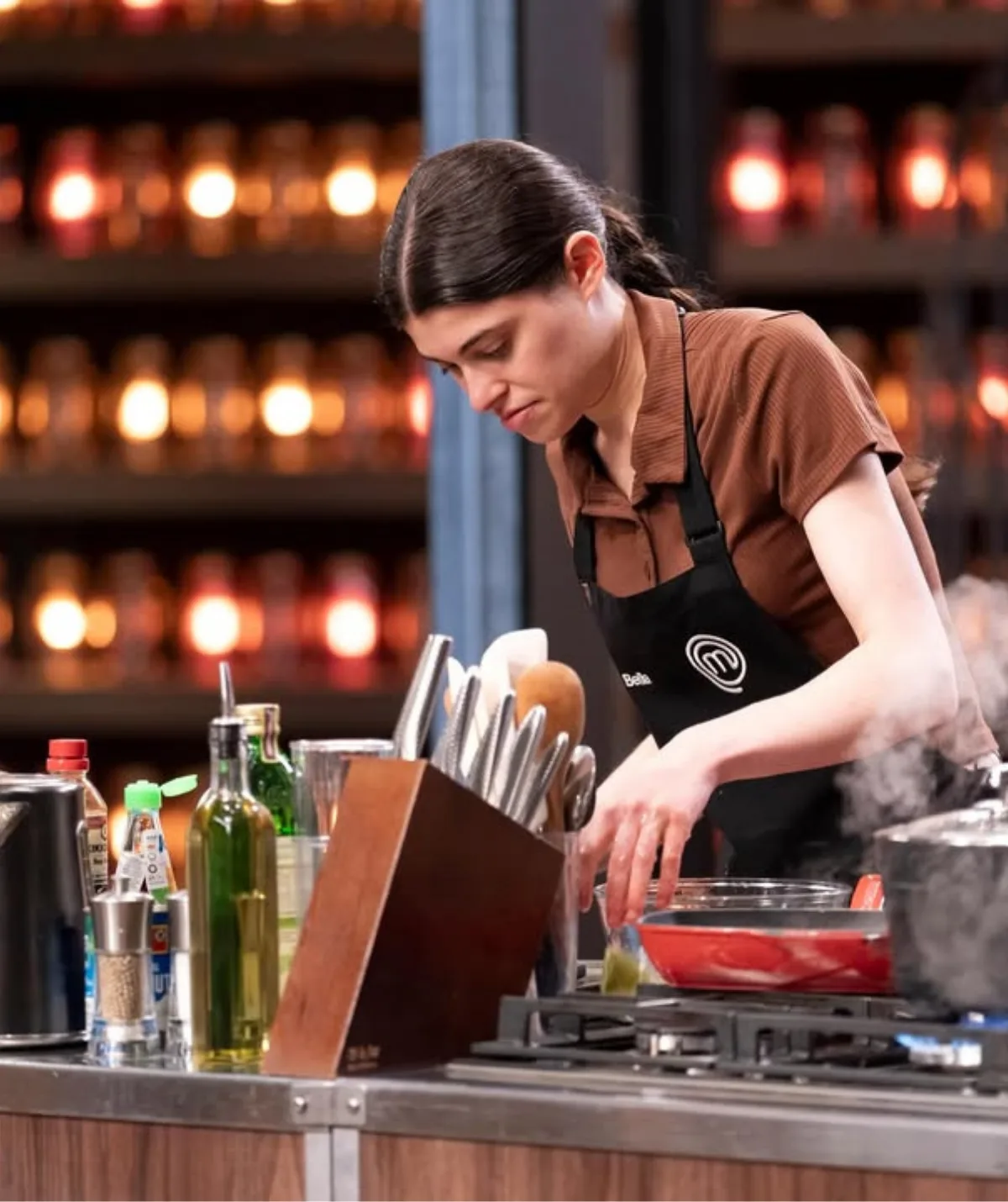 Bella di Conza in the MasterChef Australia kitchen cooking over a steaming red pan.