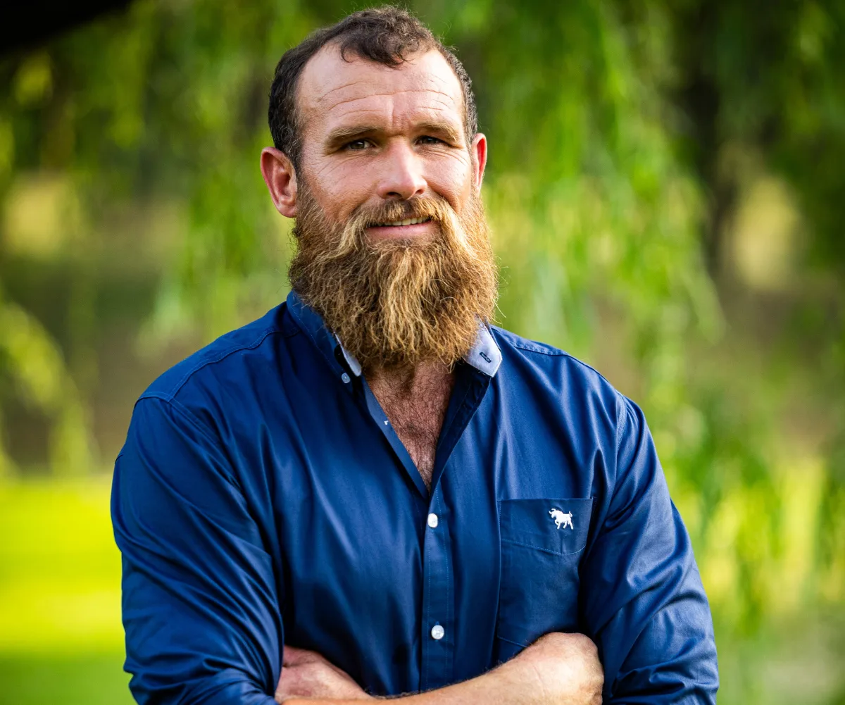 Farmer Wants A Wife Jason stands in blue shirt with arms crossed smiling