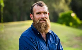 Jason, in a blue shirt, stands in front of a grassy background