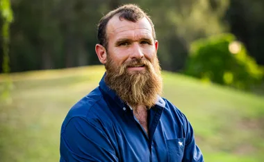 Jason, in a blue shirt, stands in front of a grassy background