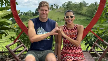 A man and woman next to each other making the heart symbol with their hands.