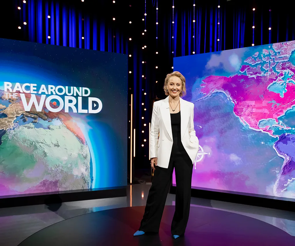 Zan Rowe, in a white jacket, stands on the set of Race Around The World