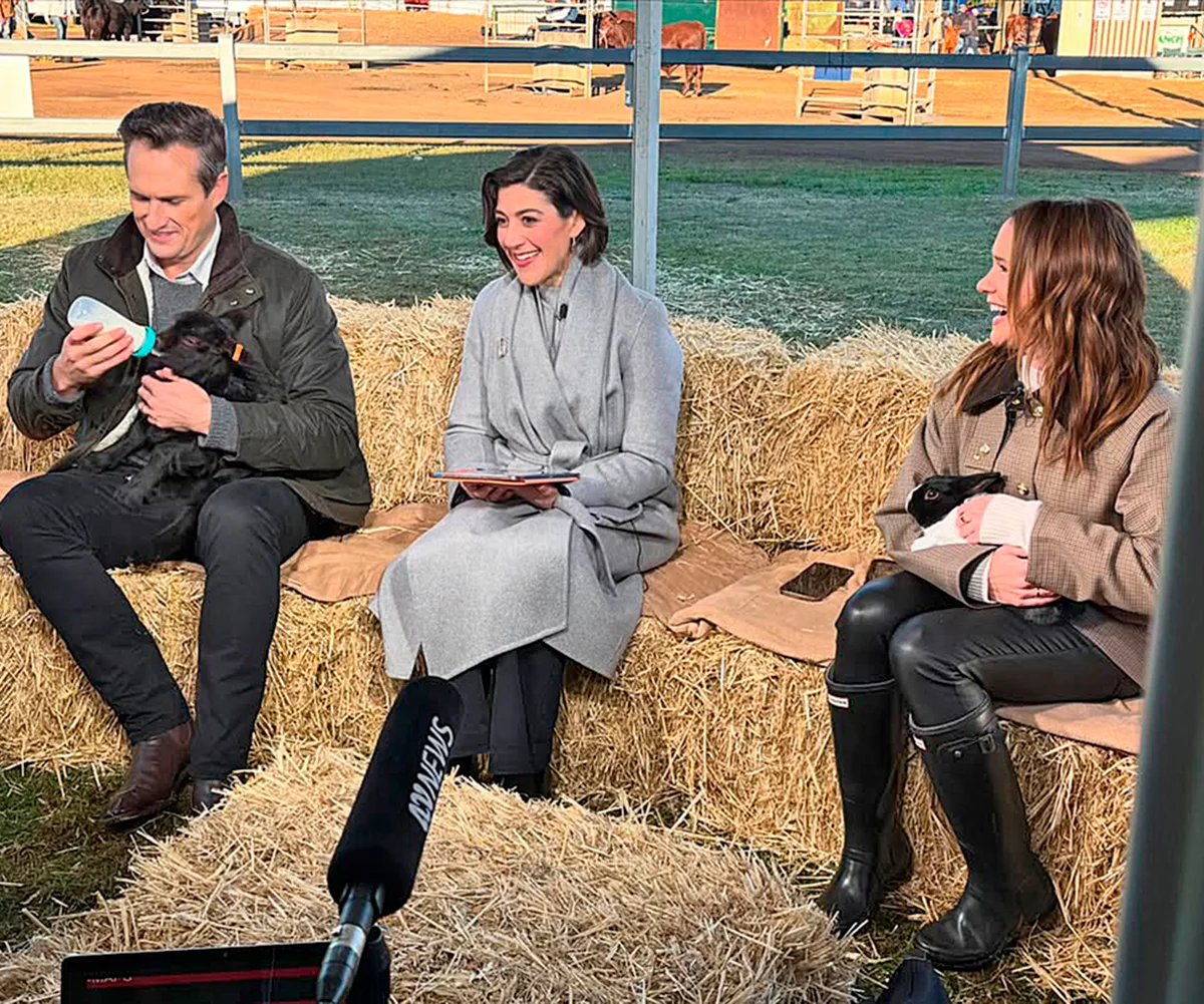 James sits on a bale of hay feeding a baby animal from a bottle