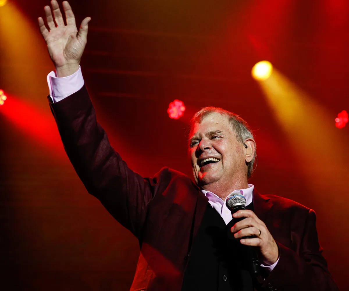 John Farnham on stage in 2019, holding microphone, one hand raised in the air