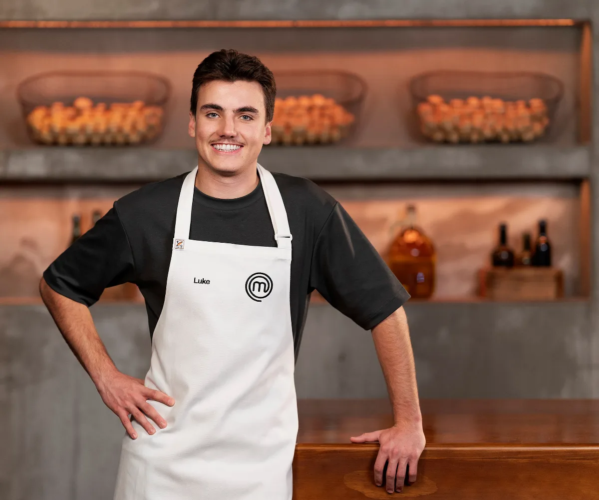 Luke Harris in the MasterChef Australia kitchen wearing a black t shirt and white apron.