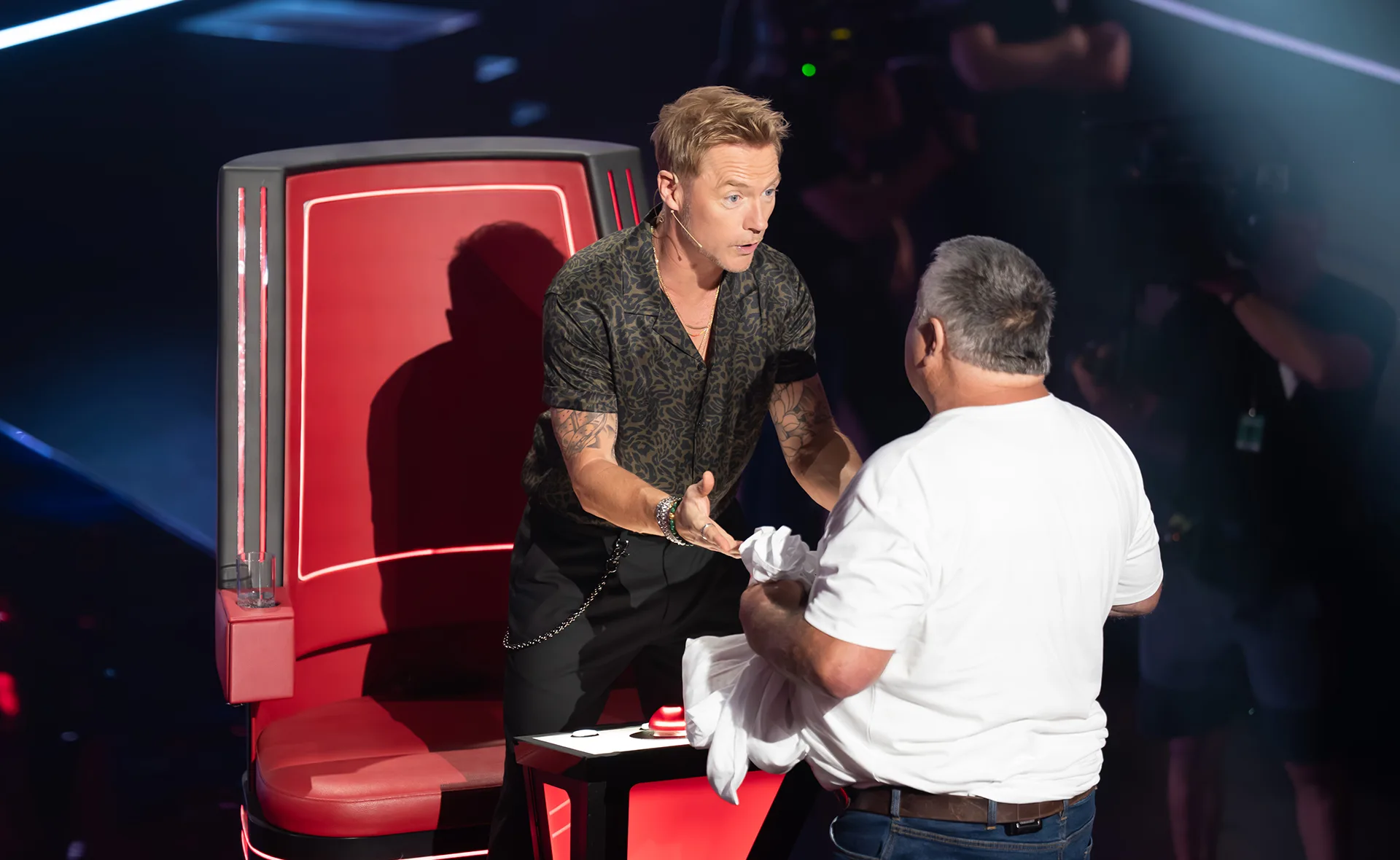 Ronan, standing up in front of his red chair, talks to Rodney