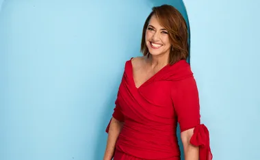 Lisa, in a red dress, stands in front of a blue background