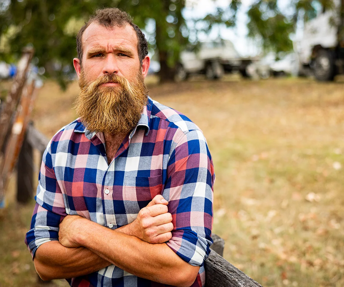 Jason, wearing a checked shirt, stands with folded arms